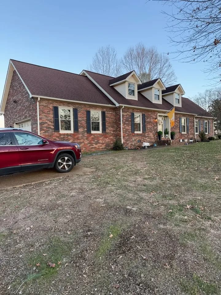 Brick cape cod house with dormers and a red SUV in the yard, Carthage