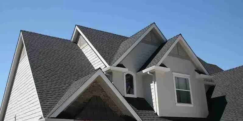 Gabled two-story house with gray architectural shingles and white siding against a blue sky