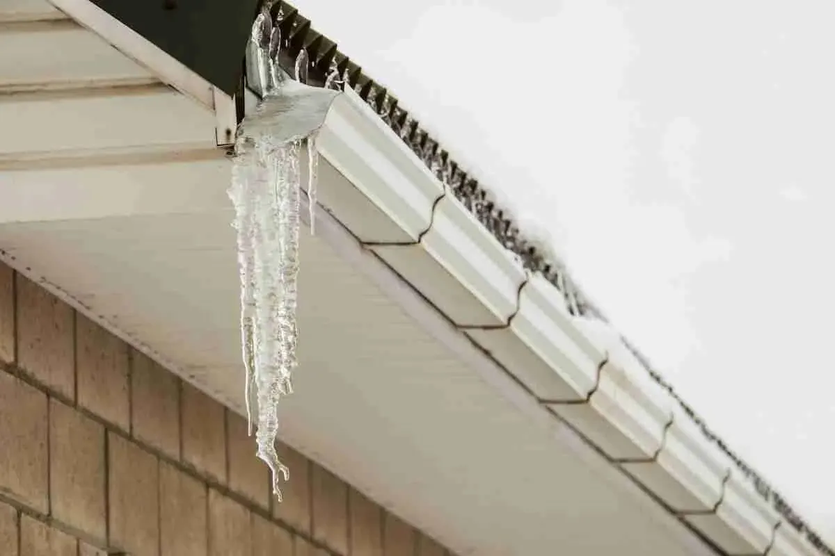Icicles hanging from a white gutter on a house with shake siding