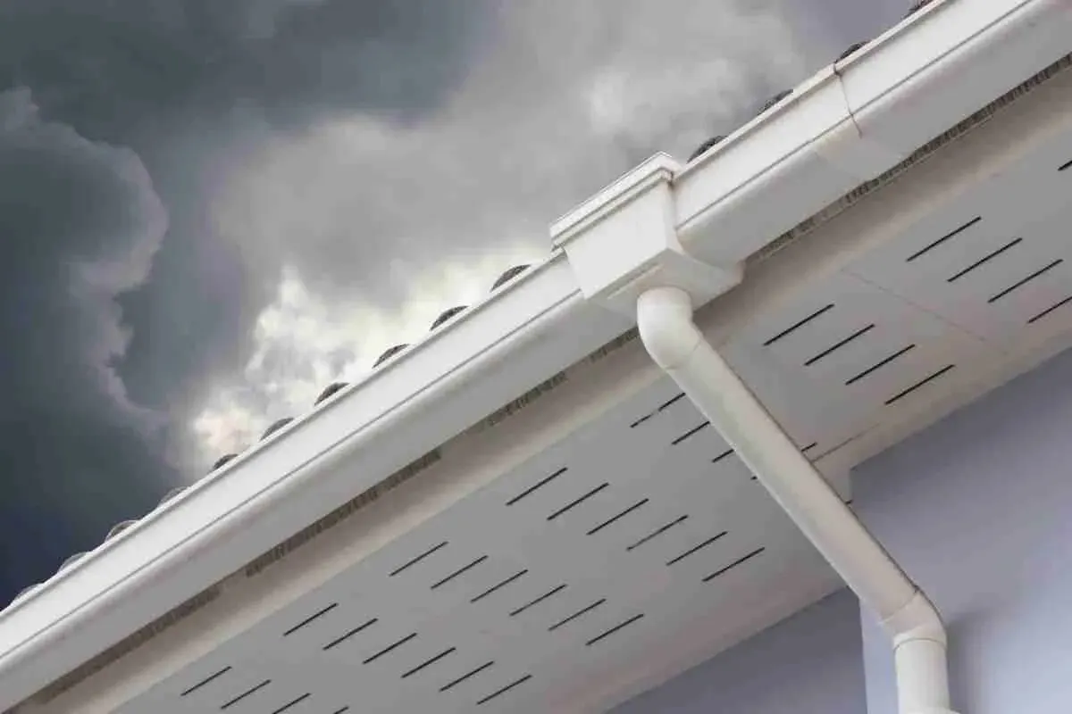 White gutter and downspout under a stormy gray sky