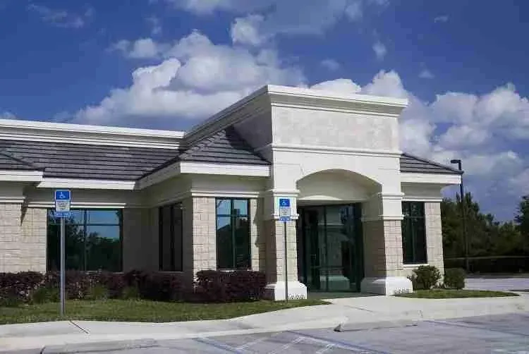 Single-story stone commercial office building with a shingle roof and parking lot