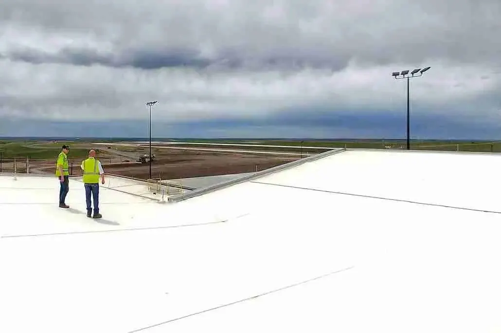 Two workers in safety vests walking on a white single-ply commercial roof