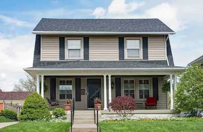 Two-story house with tan siding, dark shutters, and a covered front porch