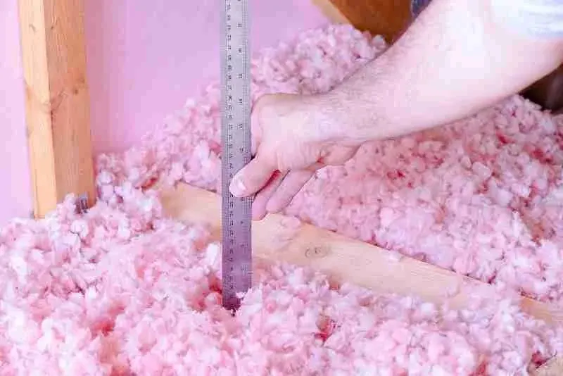 Hand holding a ruler in pink attic insulation to measure its depth