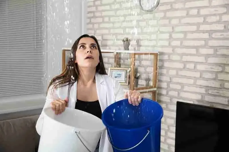 Woman catching water from a ceiling leak with two buckets