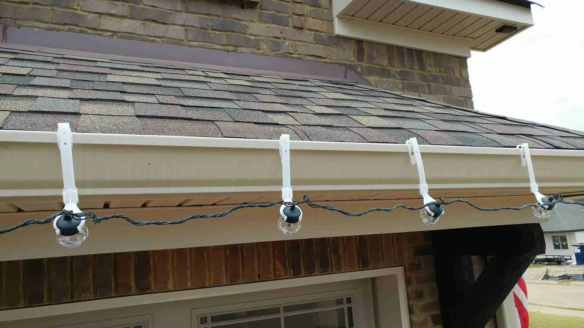 String lights clipped to a white gutter along a shingle roof edge