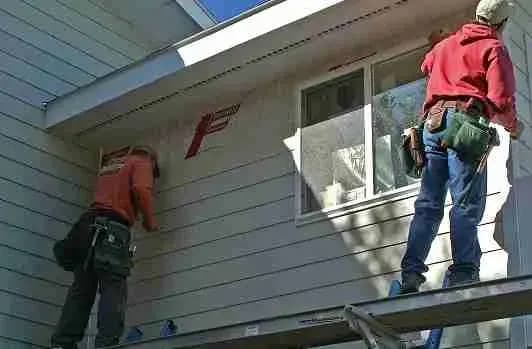 Two workers installing siding on a house wall