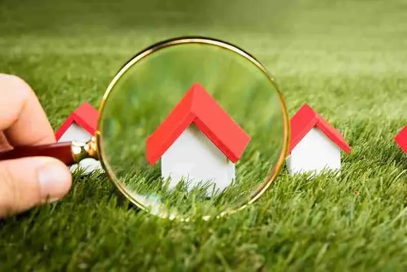 Magnifying glass held over small model houses on grass
