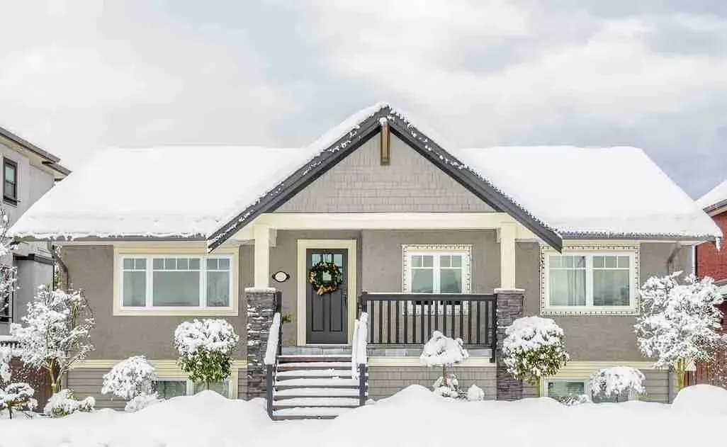 Gray house with a snow-covered roof and snowy front yard