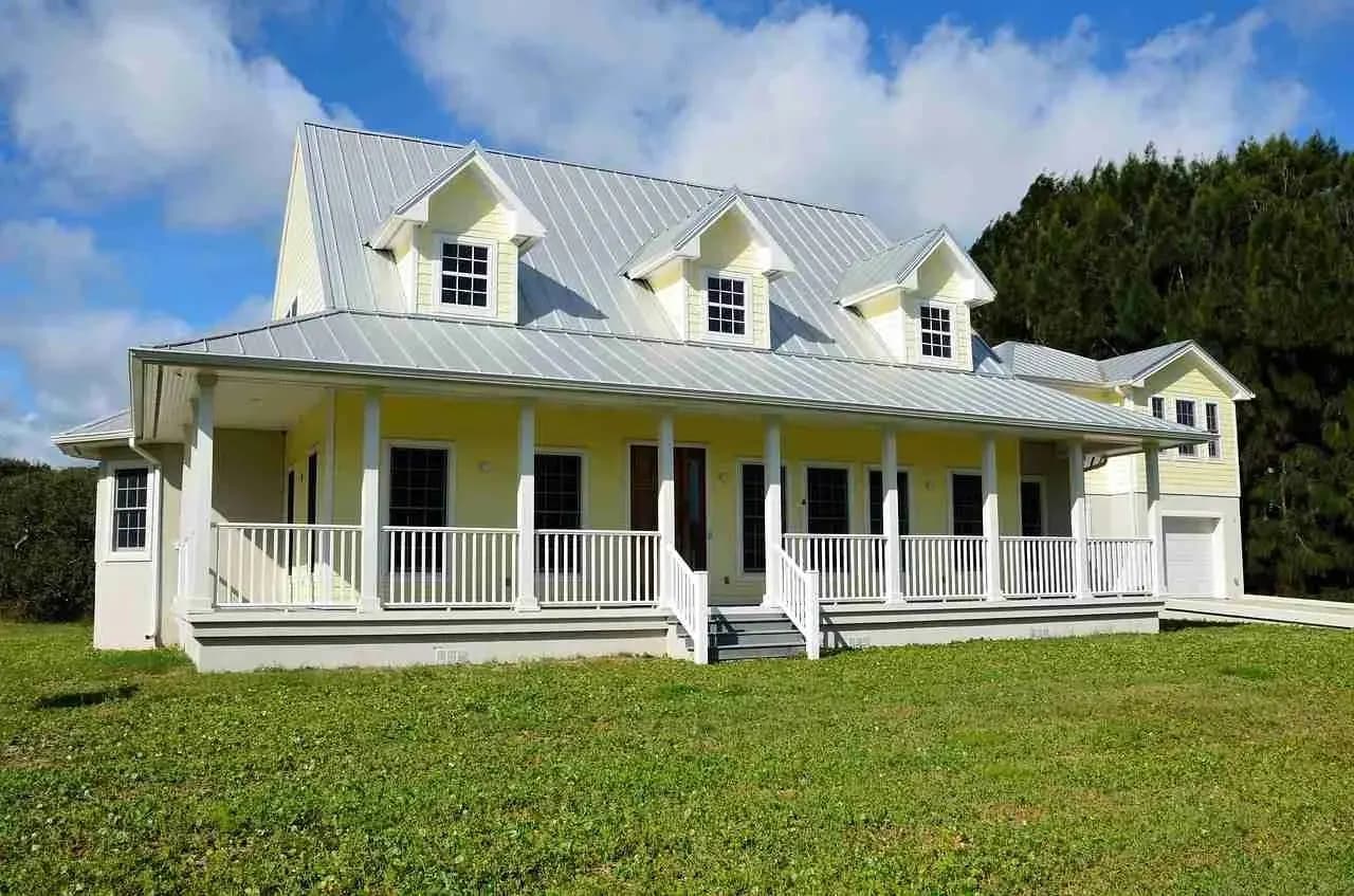 White farmhouse with a silver standing seam metal roof, three dormers and a wraparound porch