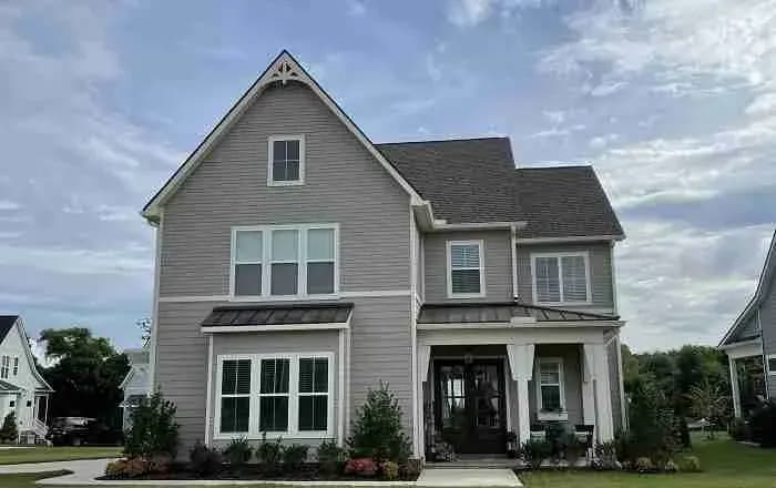Two-story gray house with a shingle roof and a small metal porch roof