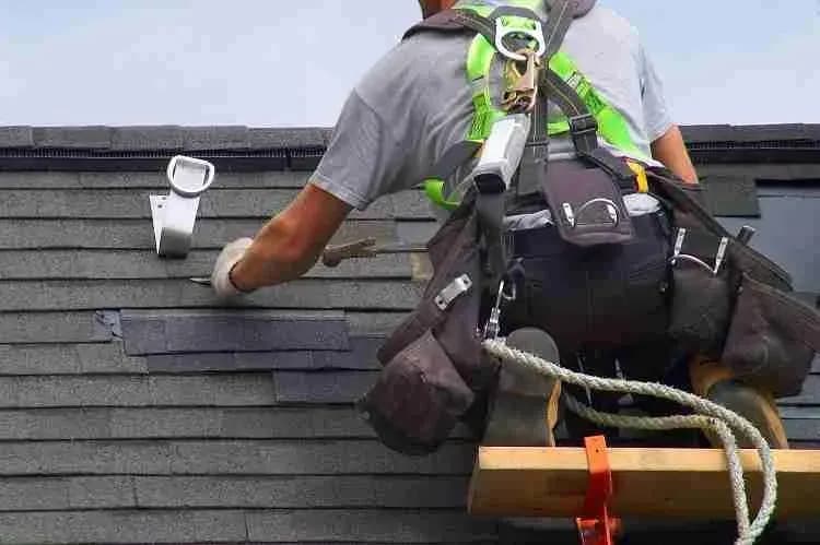 Roofer in a safety harness working on a shingle roof