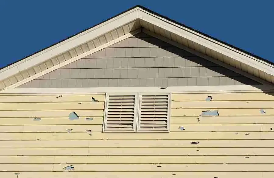 Hail-damaged vinyl siding with holes near a gable vent