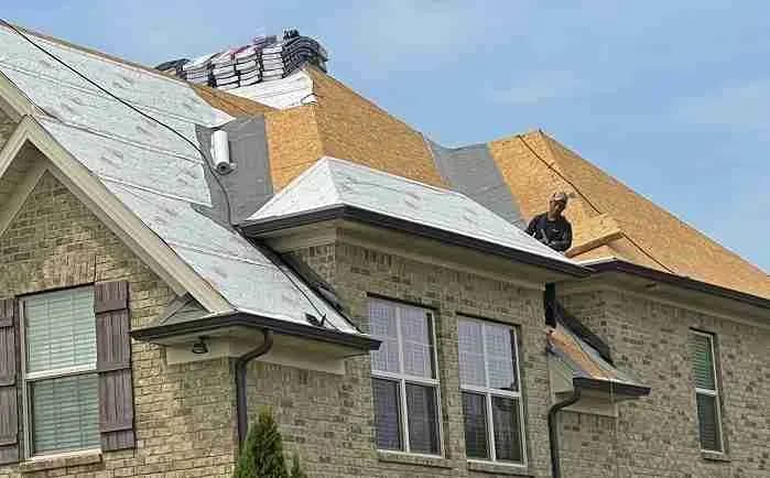 Roofer working on a brick house during a roof replacement with underlayment exposed
