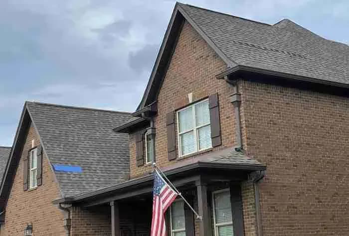 Brick house with a gray shingle roof and an American flag on the porch