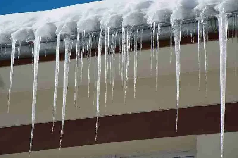 Long icicles hanging from a snow-covered roof edge and gutter