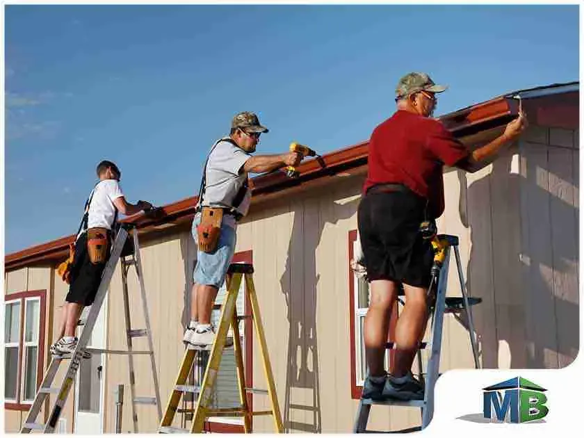 Three workers on ladders installing siding and trim on a house