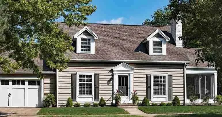 Gray cape cod house with dormers and a brown shingle roof