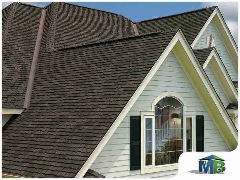 Close view of a dark shingle roof above green siding and an arched window