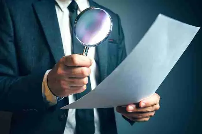 Person in a suit examining a document with a magnifying glass