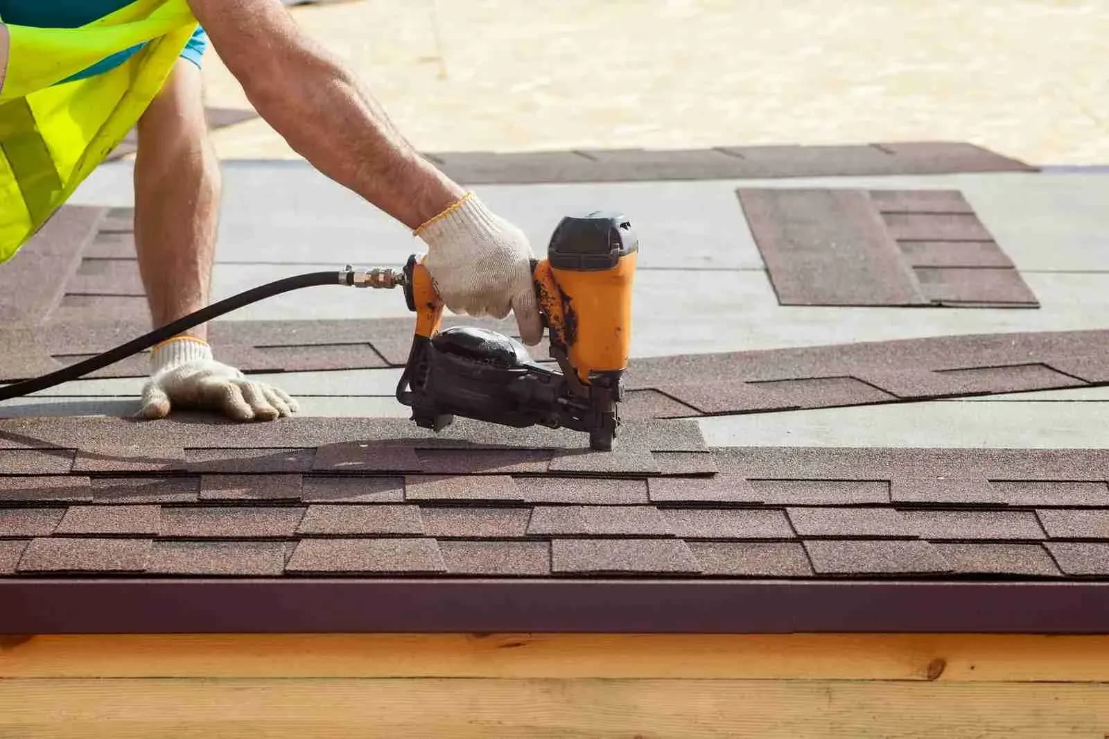 Roofer in gloves using a nail gun on brown shingles