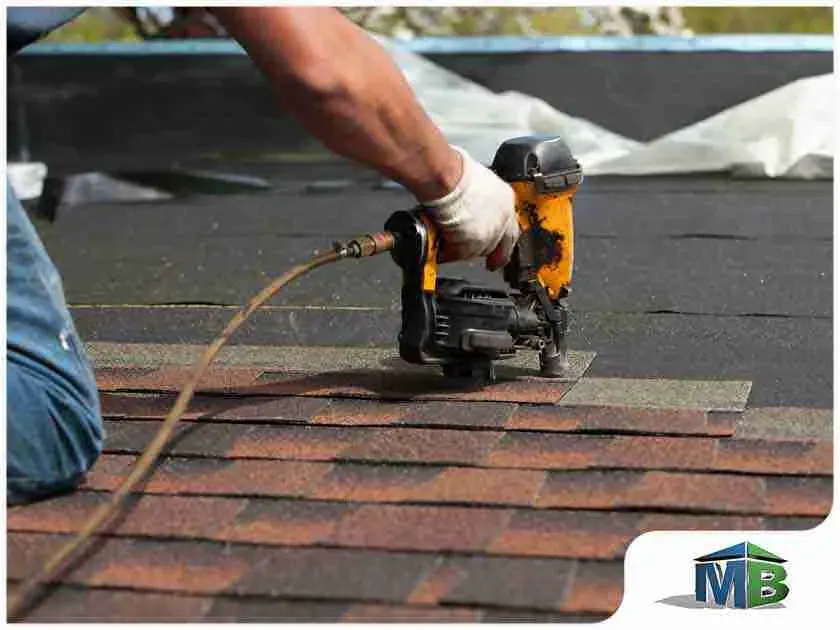 Roofer using a nail gun to install asphalt shingles