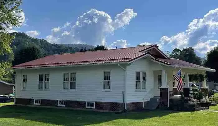 White single-story house with a red metal roof and hills behind