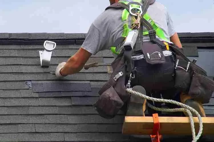 Roofer in a safety harness working on a shingle roof