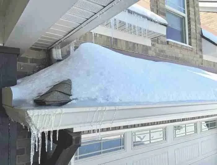 Heavy snow piled on a porch roof with icicles along the gutter