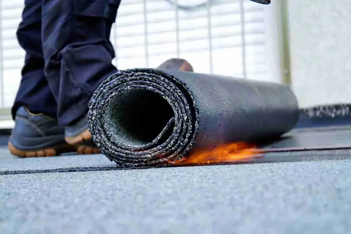 Worker unrolling torch-applied roofing membrane