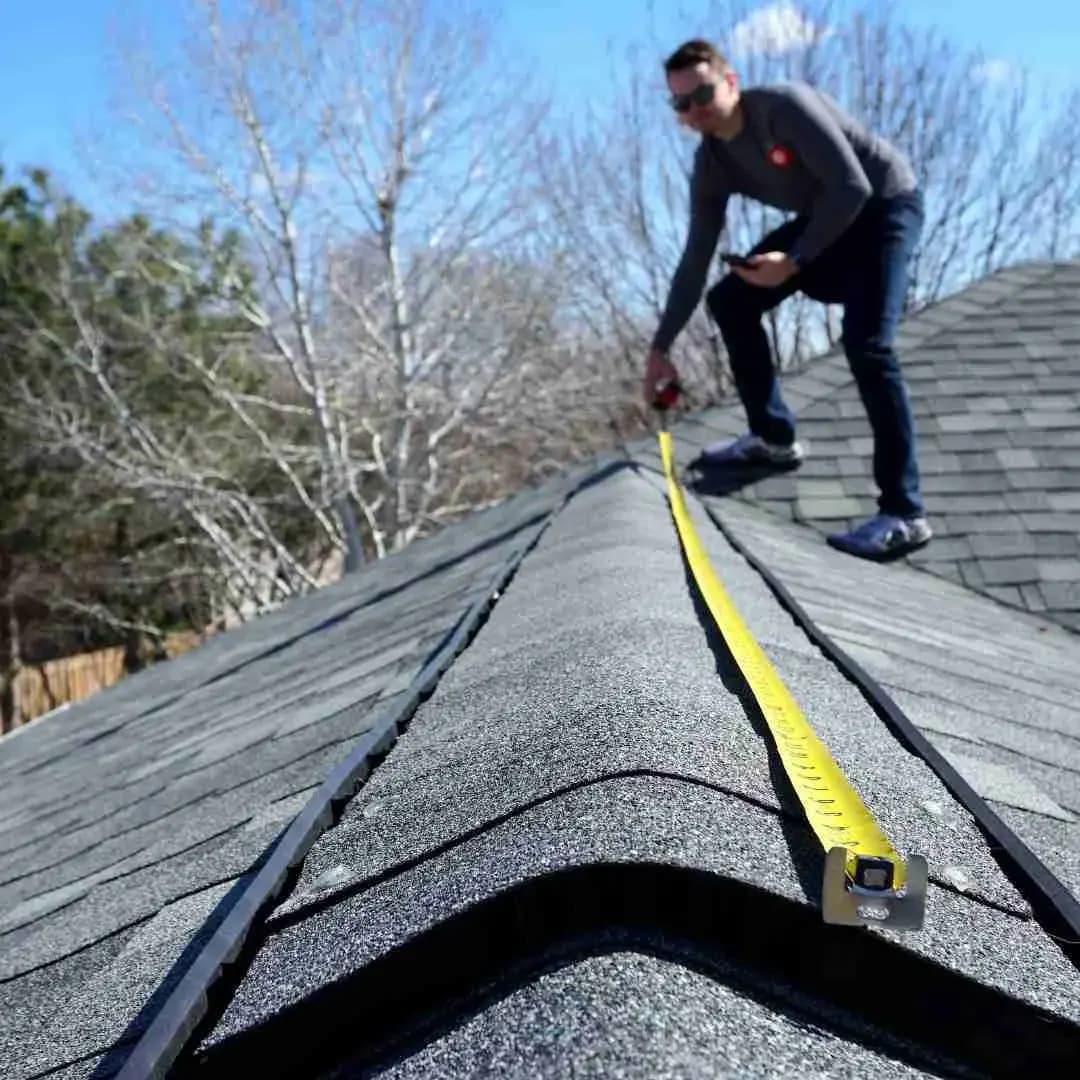 Roofer measuring a shingle roof with a tape measure