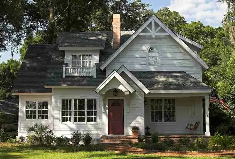 White cottage-style house with a dark shingle roof and red door