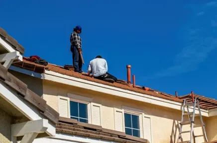 Two roofers working on a tile roof on a stucco house