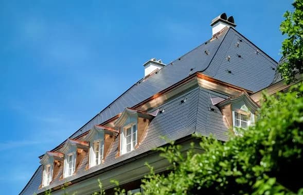 Slate roof with copper-trimmed dormers against a blue sky
