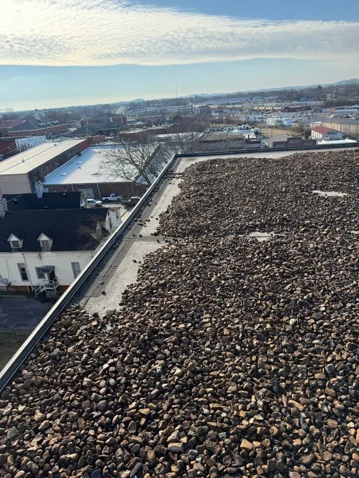 Gravel-ballasted flat commercial roof with a parapet, looking across the rooftops