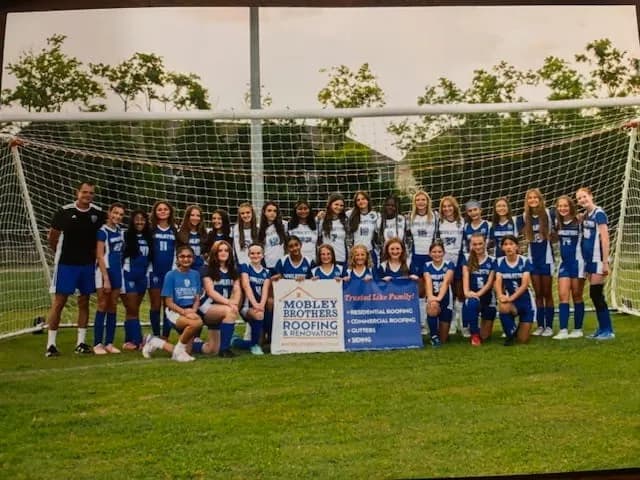 Youth soccer team posing with a Mobley Brothers Roofing banner