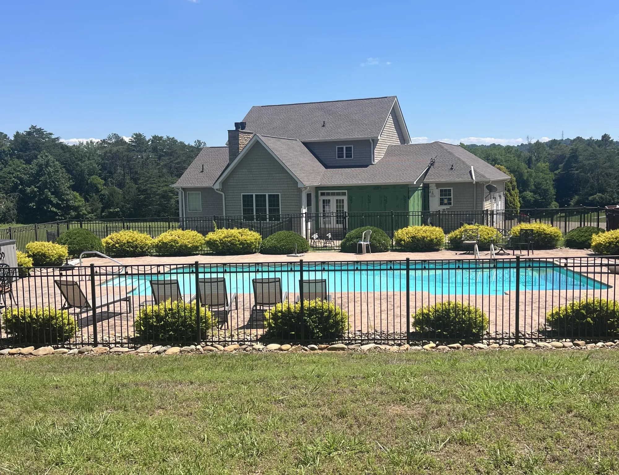 A two-story house with gray siding and shingle roofing, viewed from behind a fenced backyard pool area