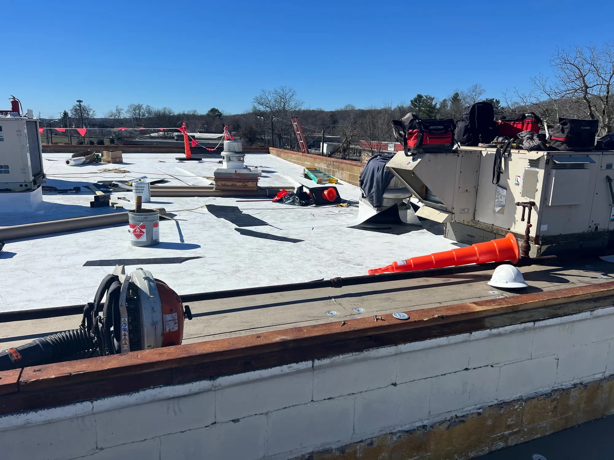 Flat commercial roof mid-installation with white membrane roofing, tools, and HVAC units under a clear sky
