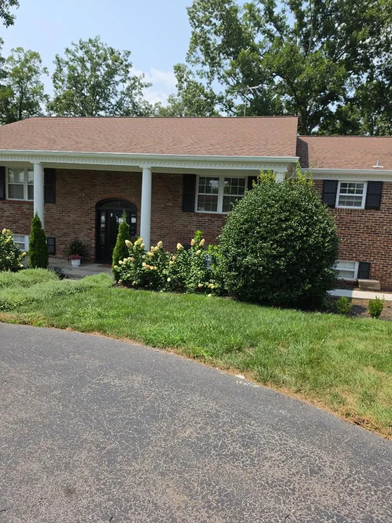 A single-story brick ranch-style home with a covered front porch, white columns, and landscaped front yard