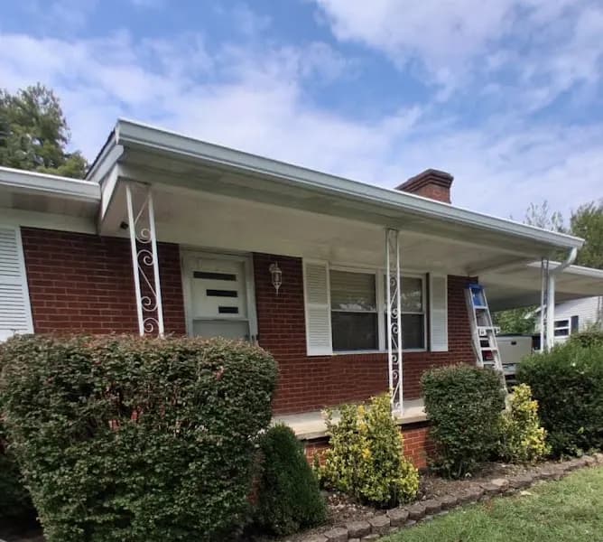 A brick ranch-style home with a covered porch, decorative iron columns, and a ladder set up against the roofline