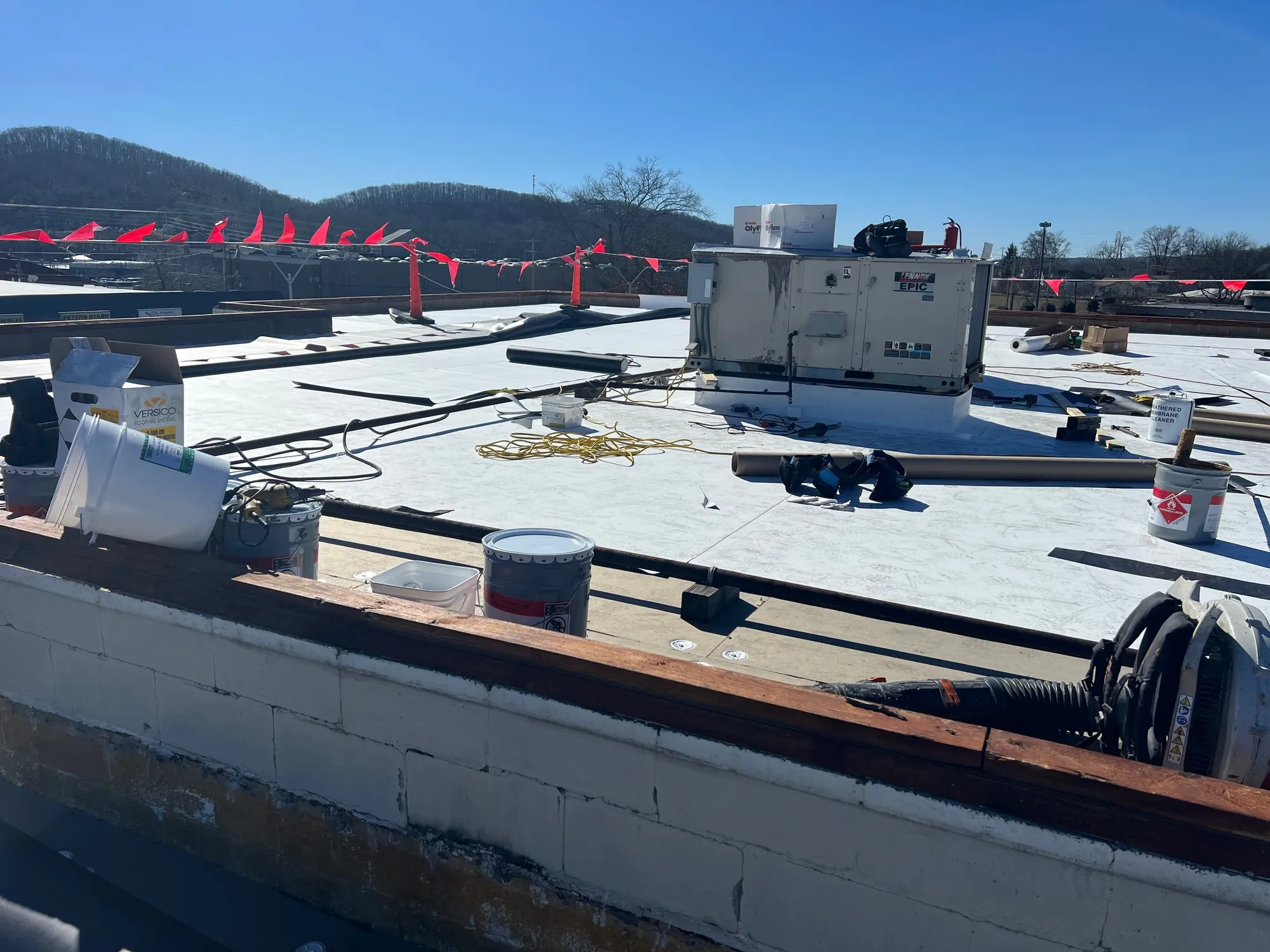 Flat commercial roof mid-installation with a rooftop HVAC unit, membrane rolls and tools, from our Knoxville office's job photos