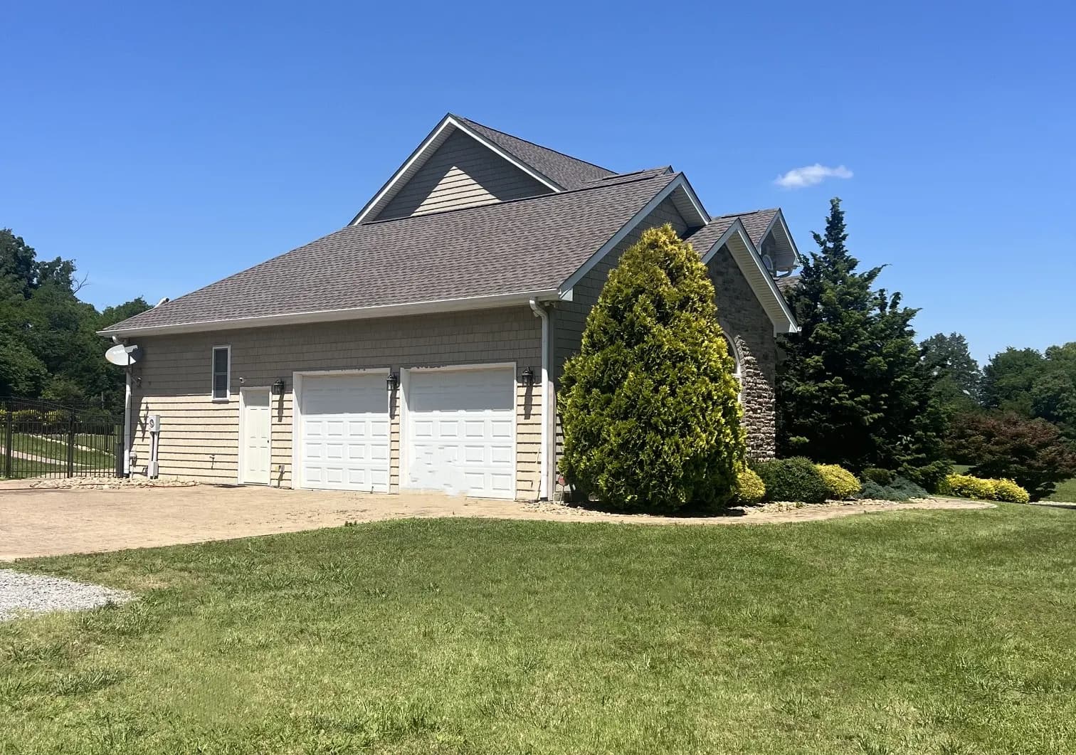 Exterior view of a house's garage and roofline featuring newly installed shingles and siding, surrounded by landscaping