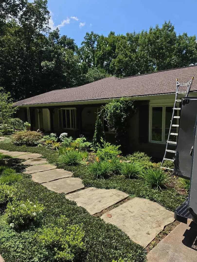 A single-story home with a shingled roof and landscaped garden, with a ladder set up against the house for roofing work
