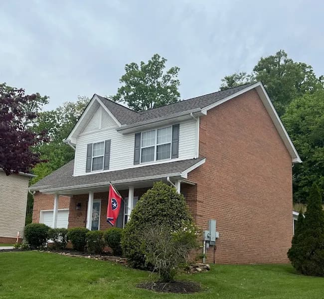 A two-story brick and vinyl-sided home with a gray shingled roof