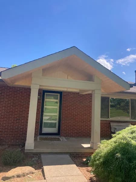 Front entrance of a brick home featuring a covered porch with a vaulted wood-paneled ceiling and white trim, showcasing renovation/roofing craftsmanship