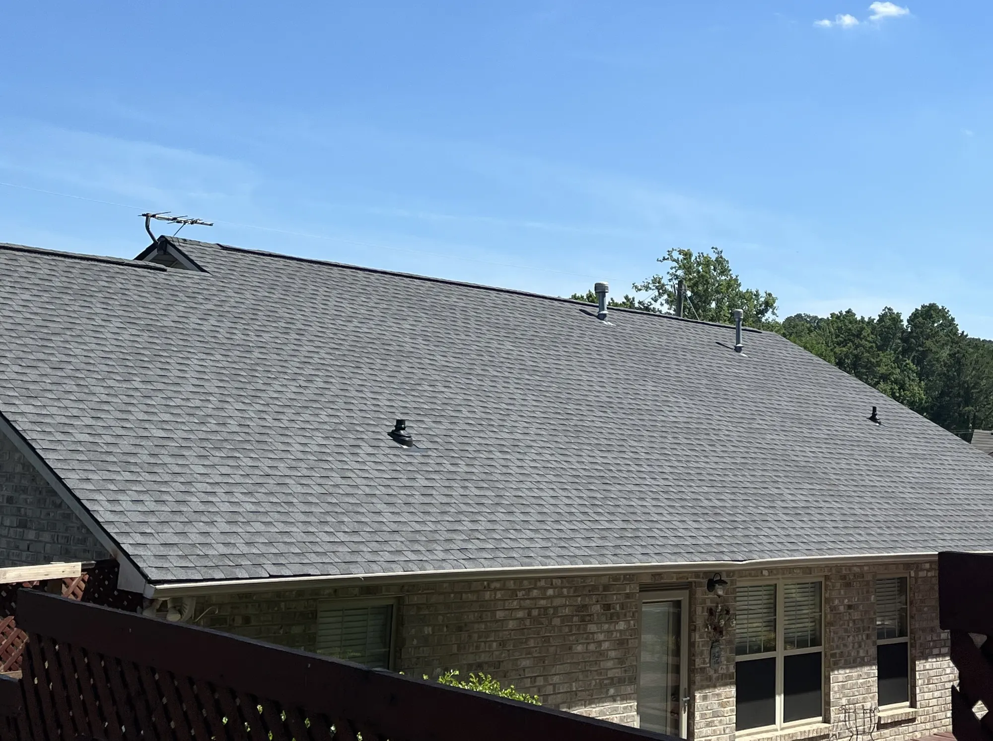 Newly shingled gray asphalt roof on a brick home, photographed from an adjacent deck under a clear blue sky