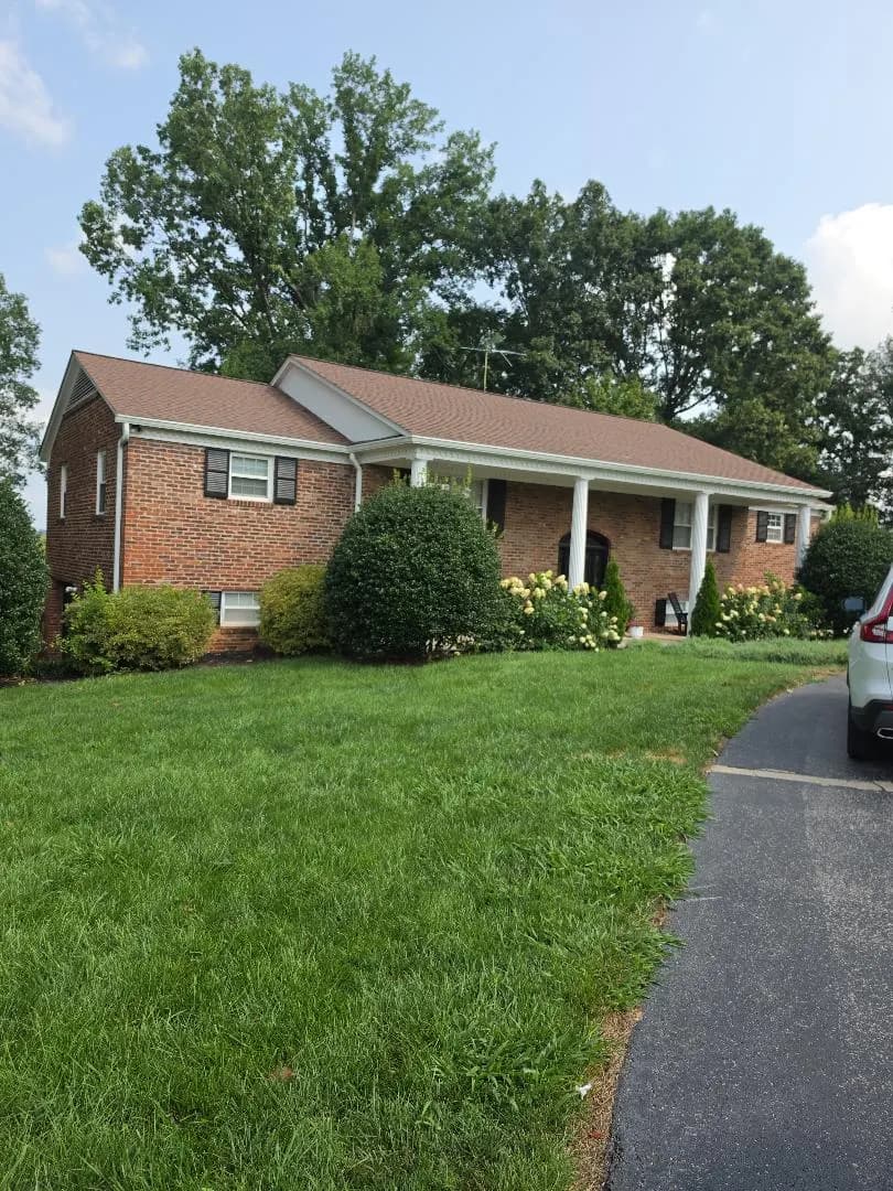 A brick two-story house with a covered front porch, white columns, and a well-maintained lawn with landscaping