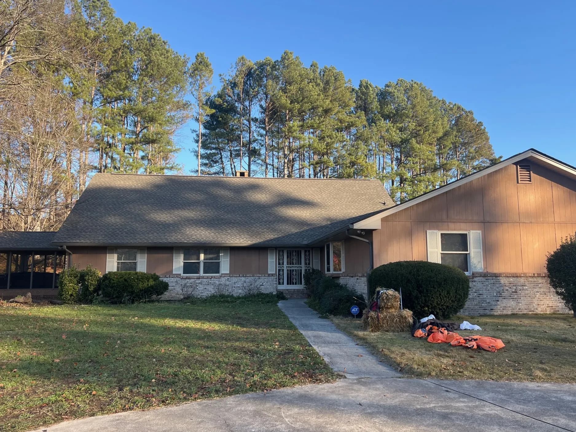 A single-story brick and wood-sided ranch home with a newly installed asphalt shingle roof, surrounded by tall pine trees