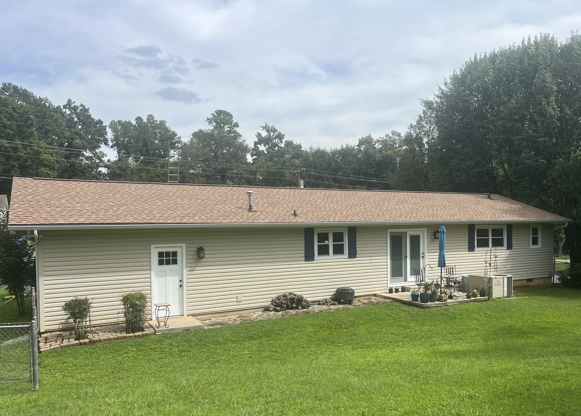 Rear exterior view of a single-story ranch home with new beige vinyl siding and a freshly installed tan shingle roof, showing a manicured backyard