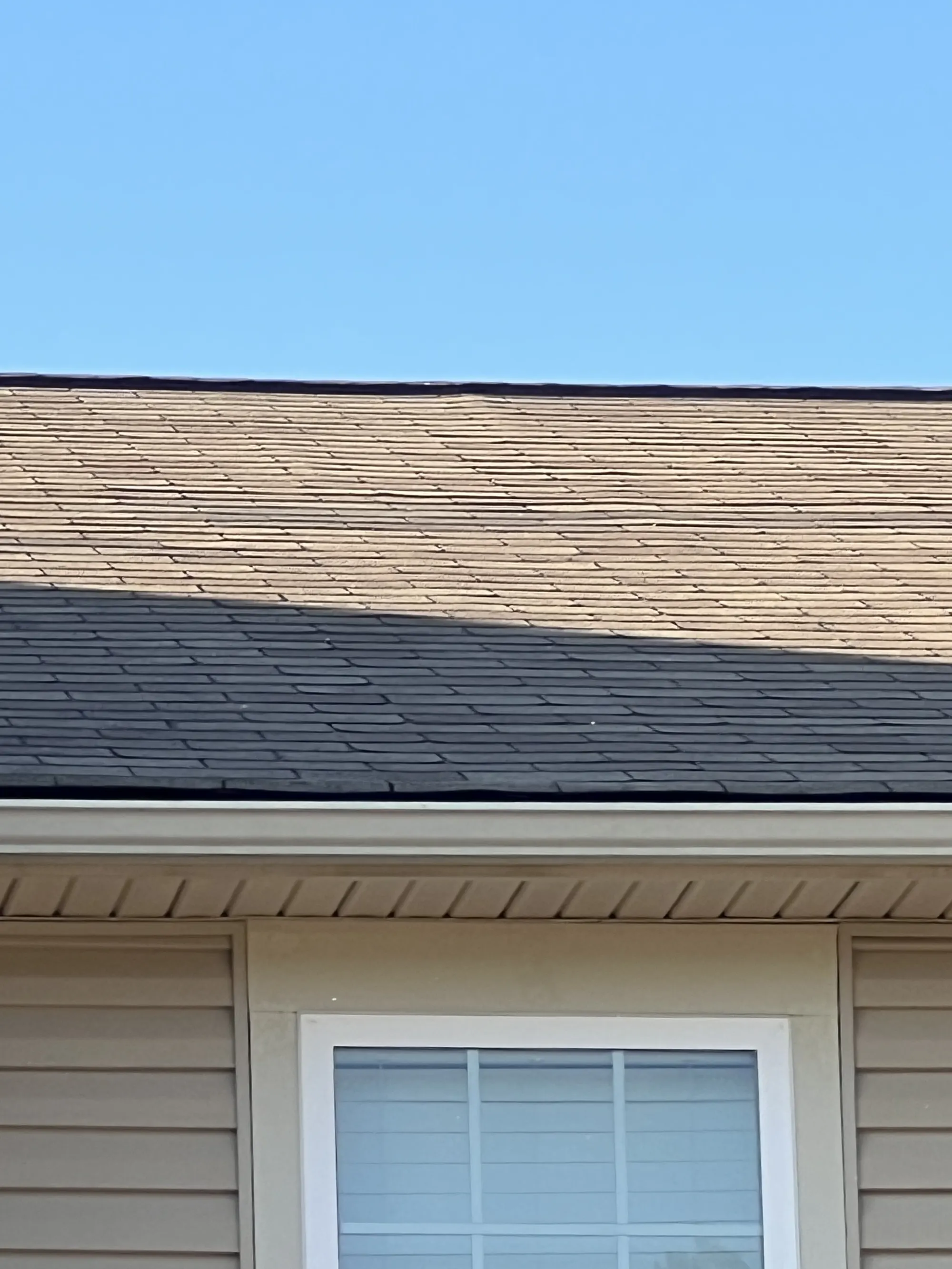 Close-up view of a residential roofline showing two different shingle colors, likely illustrating a roof repair or replacement section